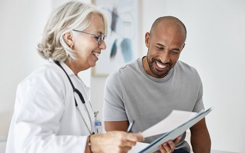 Ärztin im weißen Kittel bespricht Untersuchungsunterlagen mit einem Patienten.