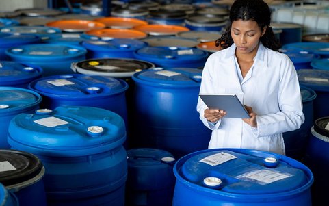 Woman with tablet in hand inspects a chemical barrel